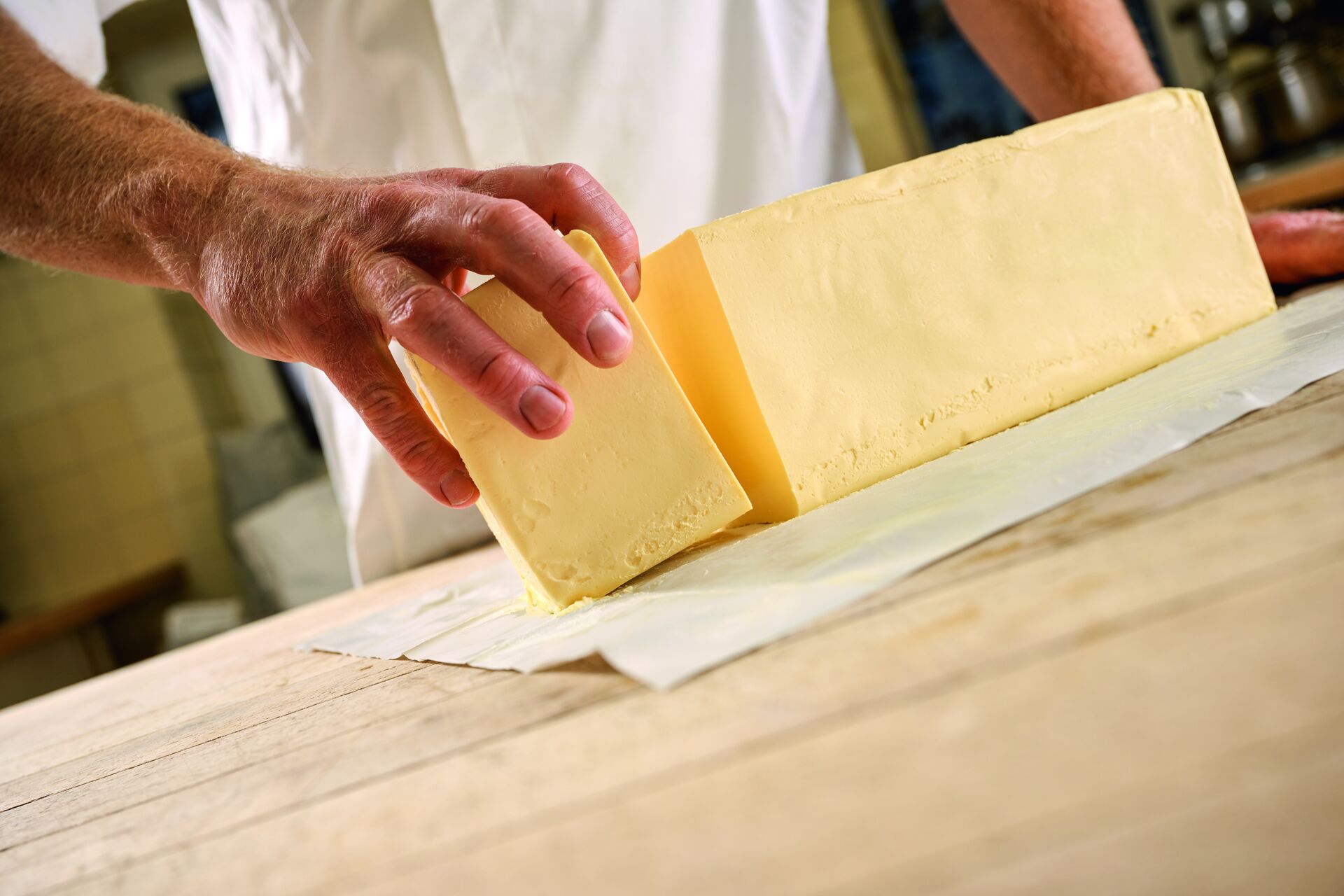 Ein professioneller Koch in einer Backstube greift mit der Hand nach einem abgetrennten Stück eines großen Blocks fester Margarine.